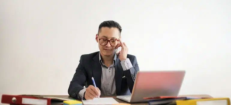 Person at a desk writing and talking on the phone 
