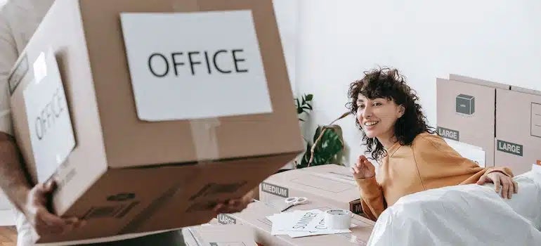 Person carrying box labeled "office" while woman watches 