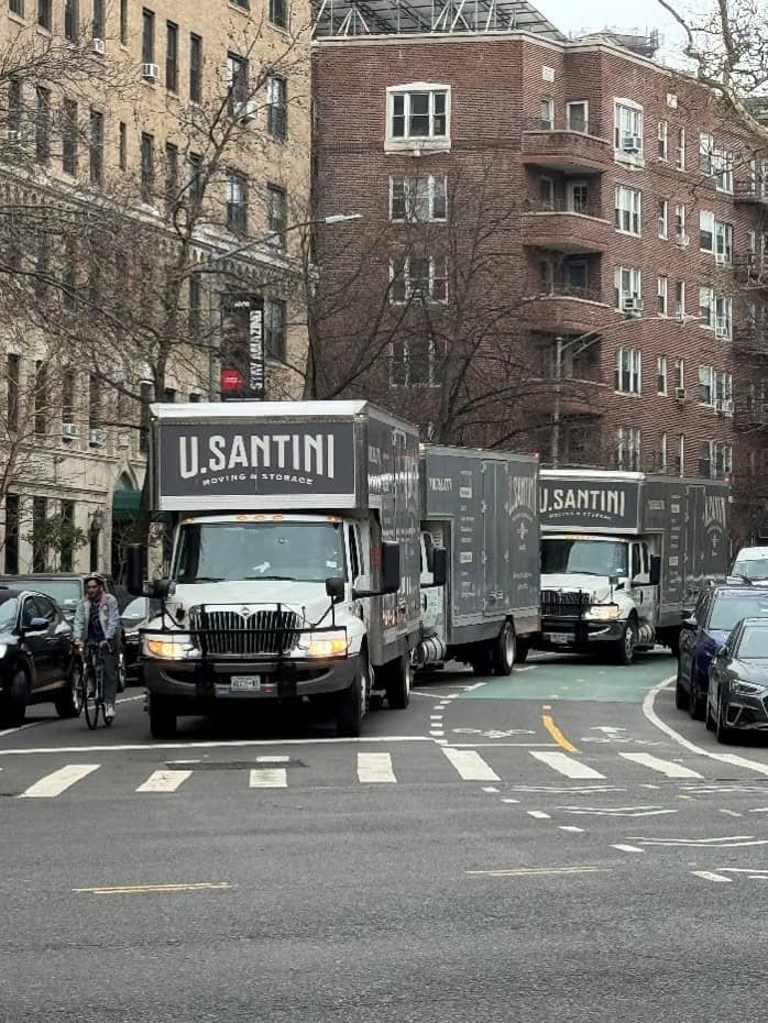 Three U. Santini Moving & Storage employees in branded jackets and caps standing in front of a company moving truck on a Brooklyn street on an overcast winter day