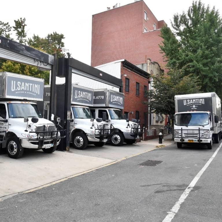 Four U. Santini Moving & Storage branded moving trucks parked outside the company's Brooklyn headquarters on a sunny day