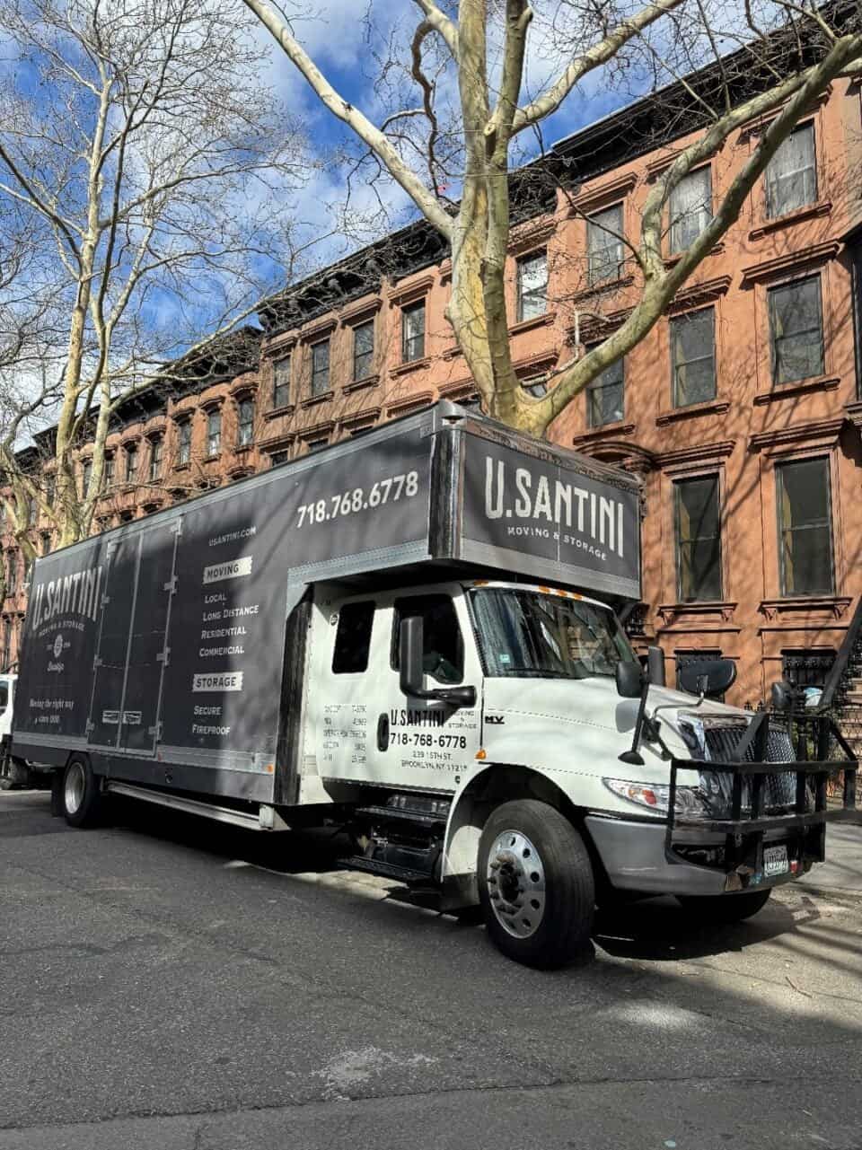 A large U. Santini Moving & Storage truck parked along a tree-lined Brooklyn street in winter, displaying the company phone number 718.768.6778 and a list of services