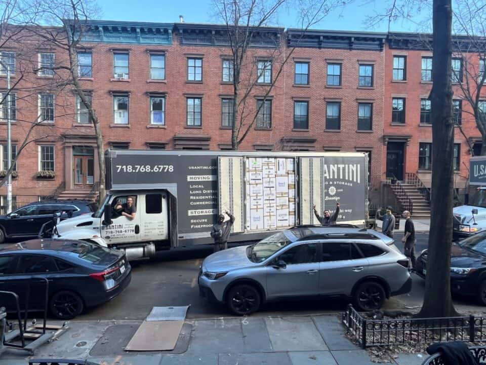 A U. Santini Moving & Storage truck with its rear doors open on a Brooklyn residential street, with crew members visible near the truck on a clear winter day