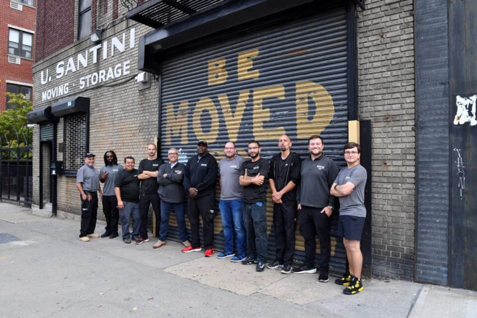 The U. Santini Moving & Storage crew of eleven employees lined up in front of the company's Brooklyn garage, featuring a gold 